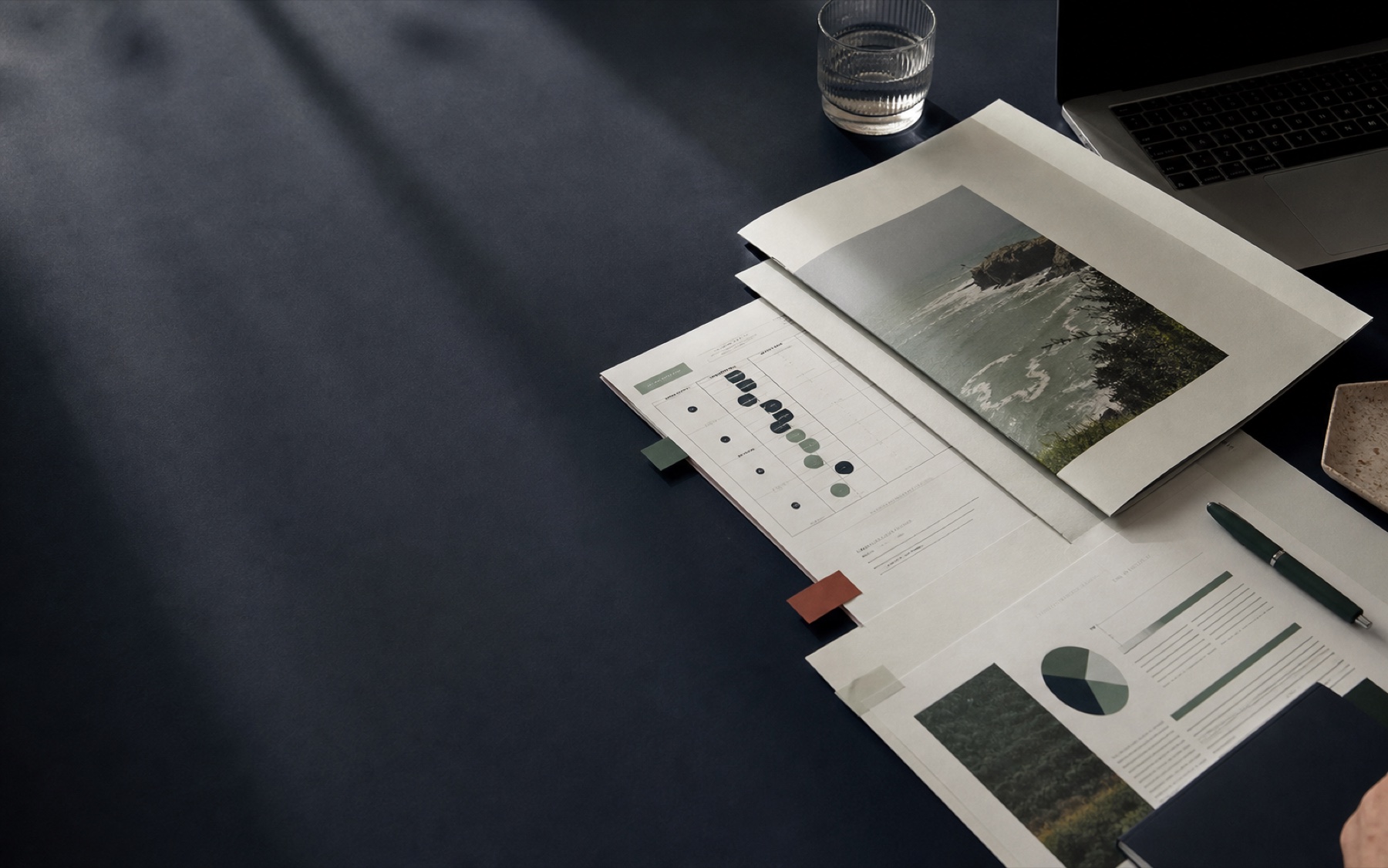 An editorial still life of printed research, a decision matrix and working materials on a dark table.